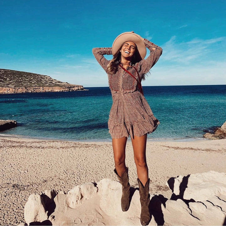 Chica en la playa vistiendo botas cowboy en ante marrón, vestido y sombrero