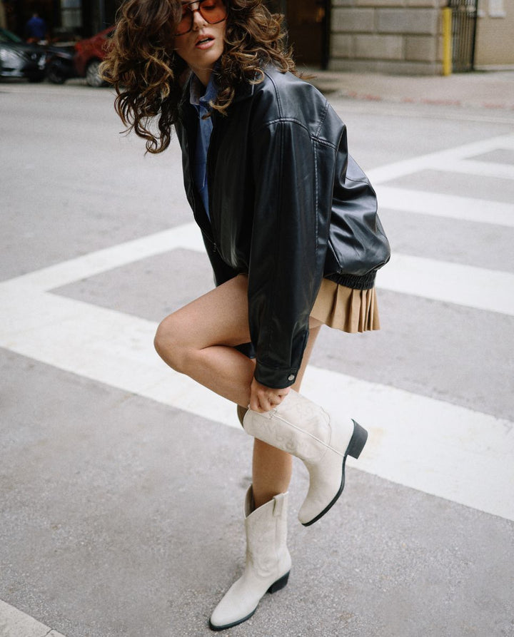 Chica con pelo rizado llevando botas cowboy blancas de caña media en la calle