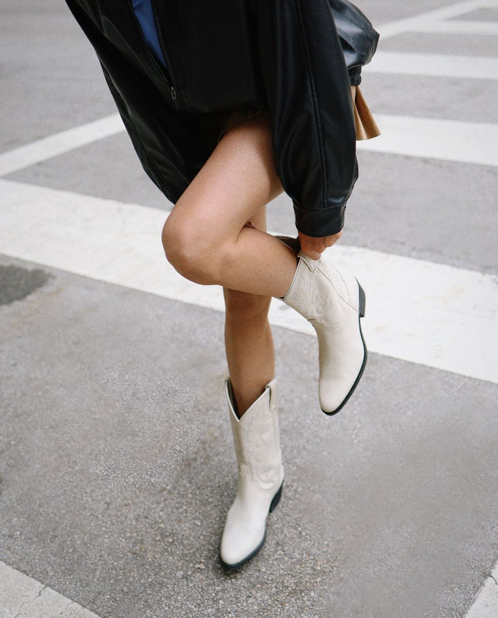 Mujer con par de botas cowboy blancas de caña media en la calle