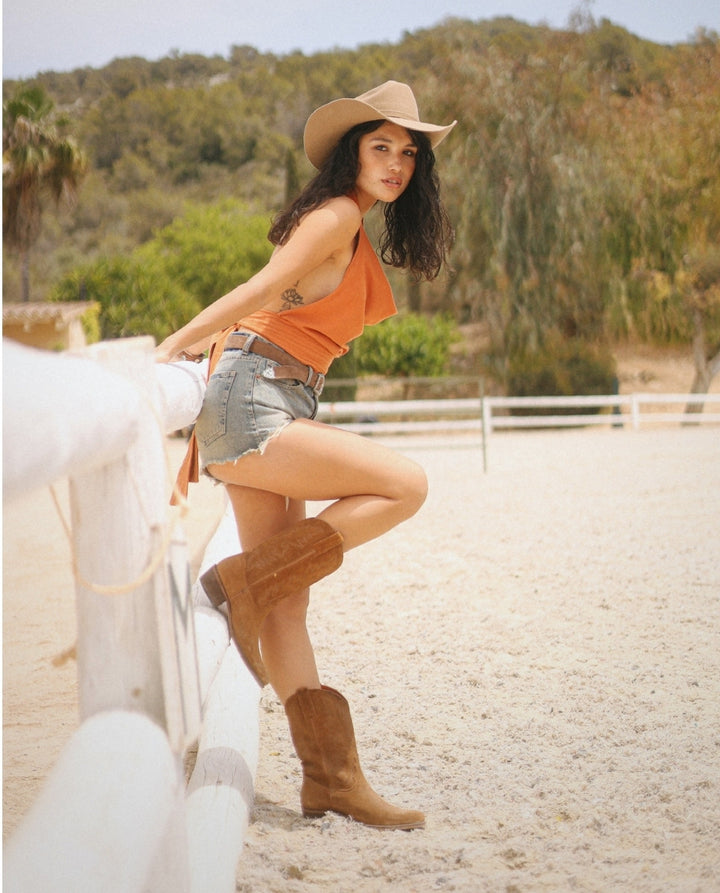 Chica con shorts jeans y botas cowboy en ante marrón caña media