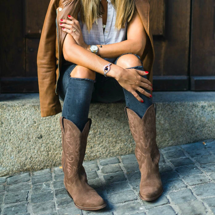 Mujer con botas texanas marrones y jeans rotos media caña
